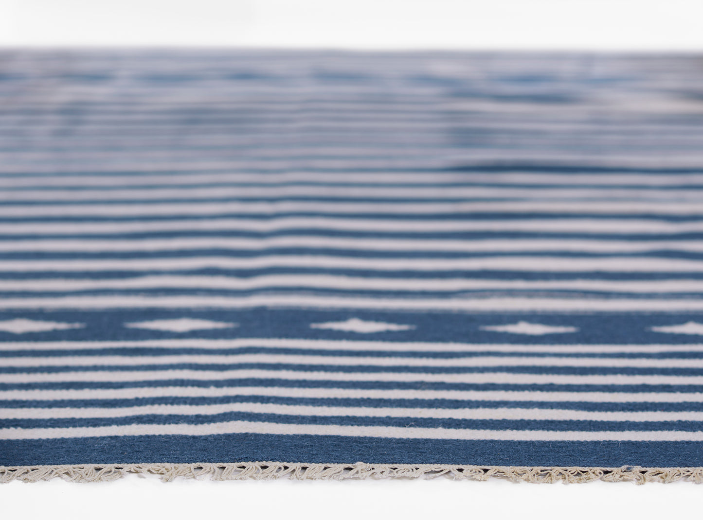 Blue and white striped woven rug close-up with fringe along the edge.