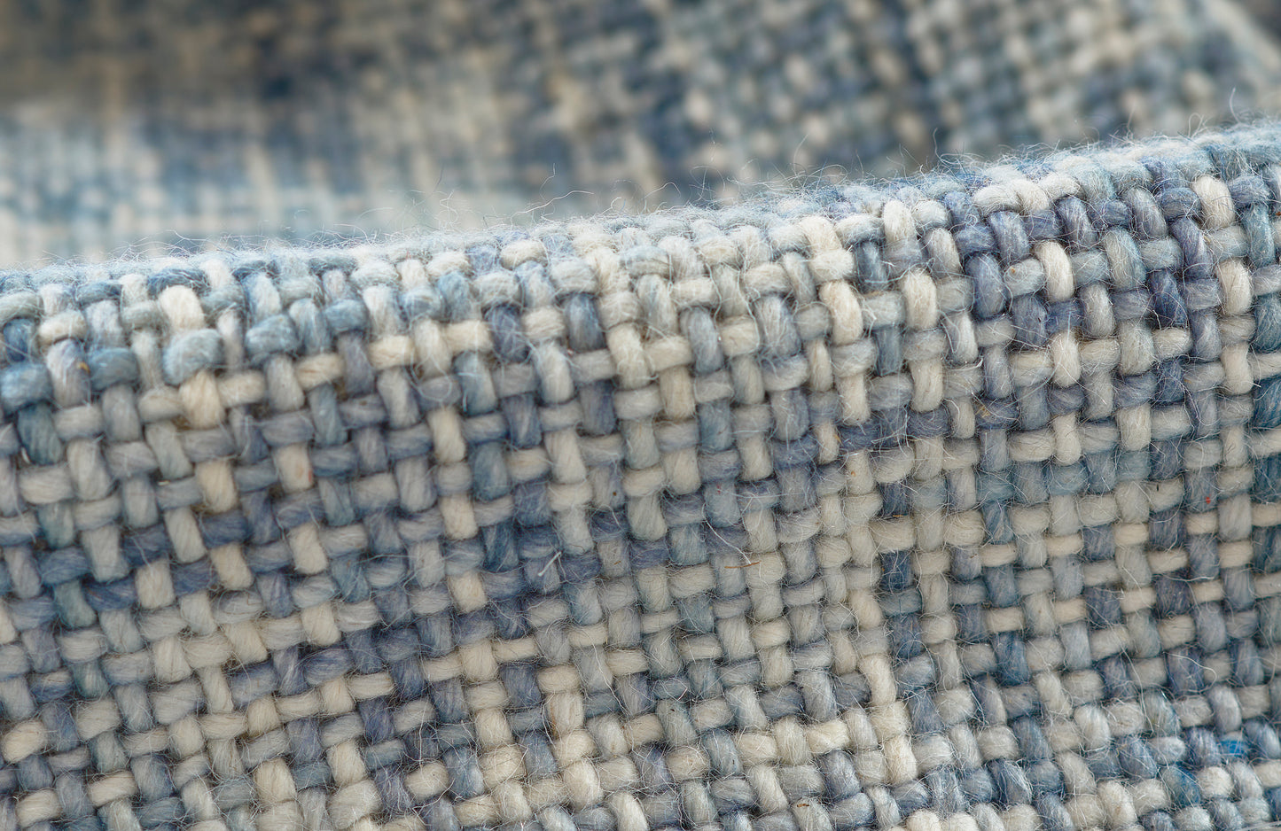 Close-up of a blue and ivory woven rug texture with thick yarns and a tight basket-weave pattern.
