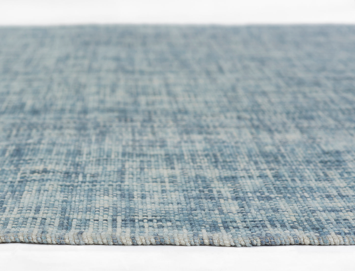 Blue woven rug close-up showing denim tones, textured loop pile and light beige edge fringe.