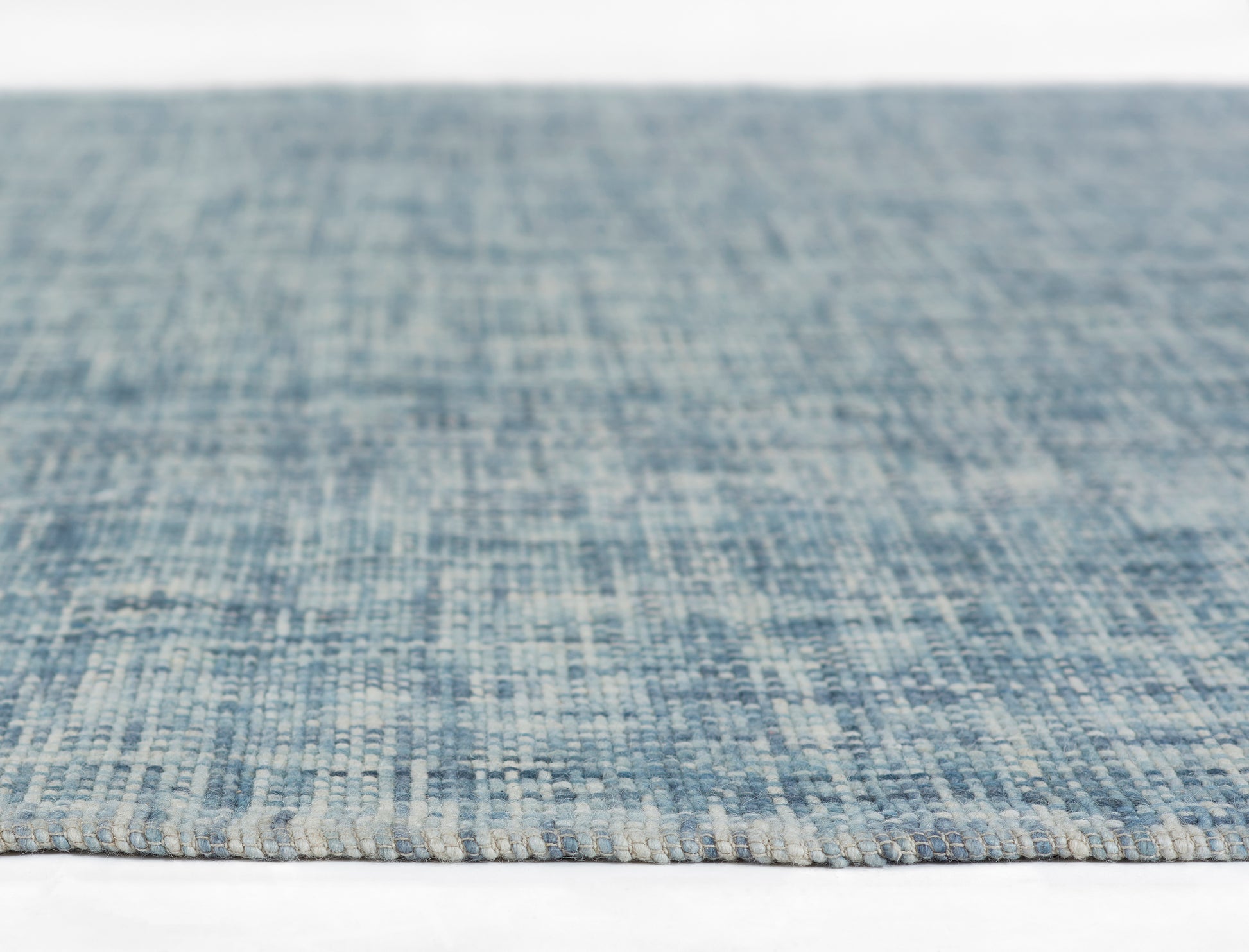 Blue woven rug close-up showing denim tones, textured loop pile and light beige edge fringe.