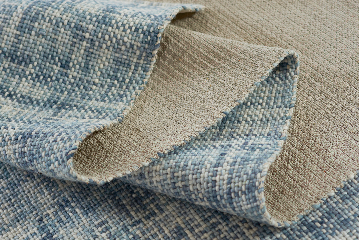 Blue and beige woven rug with a speckled blue top, beige reverse, and textured loop weave with rolled edge.