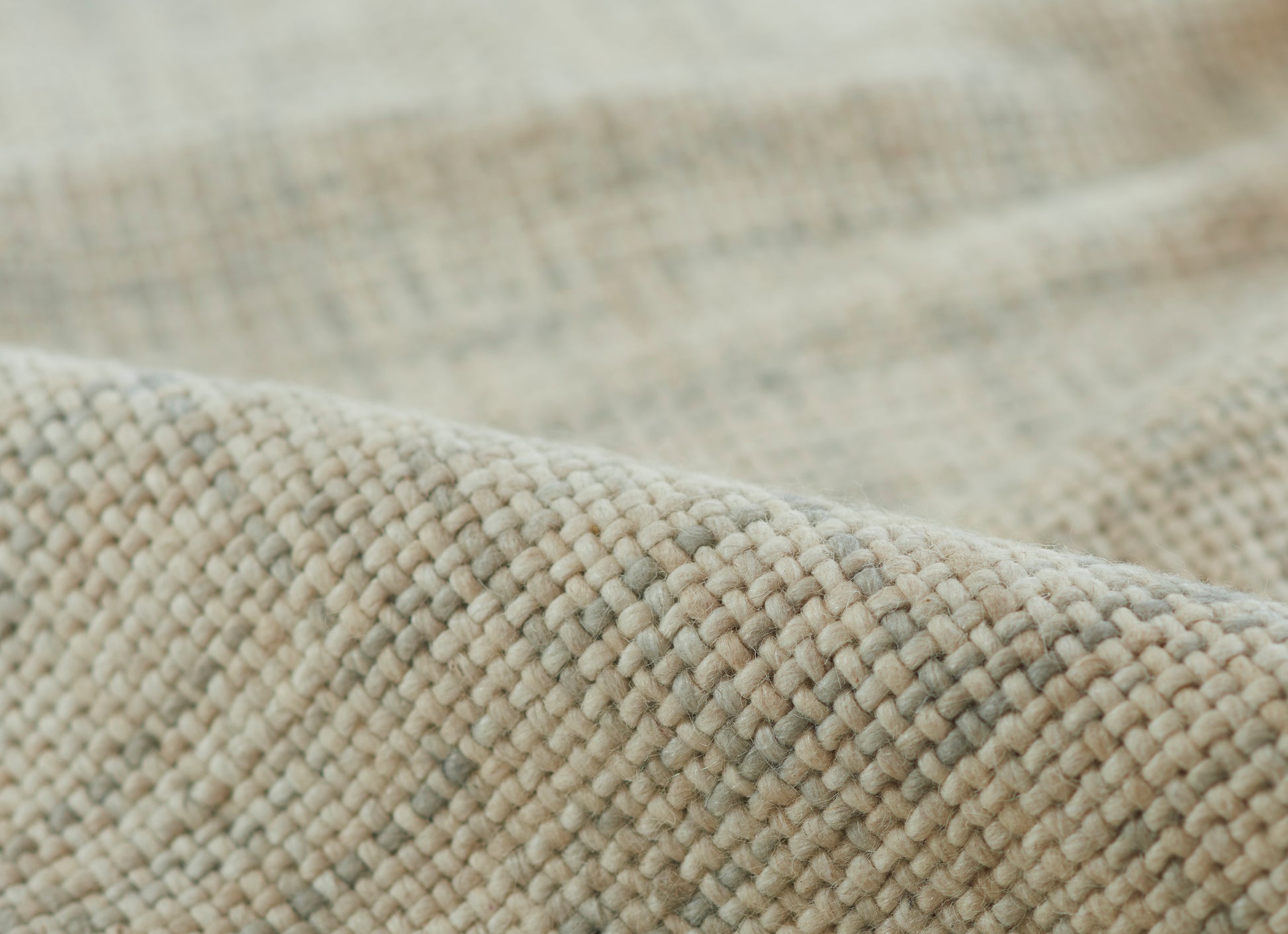 Close-up of beige-gray chunky woven fabric; soft textured textile, ideal for throws or rugs.