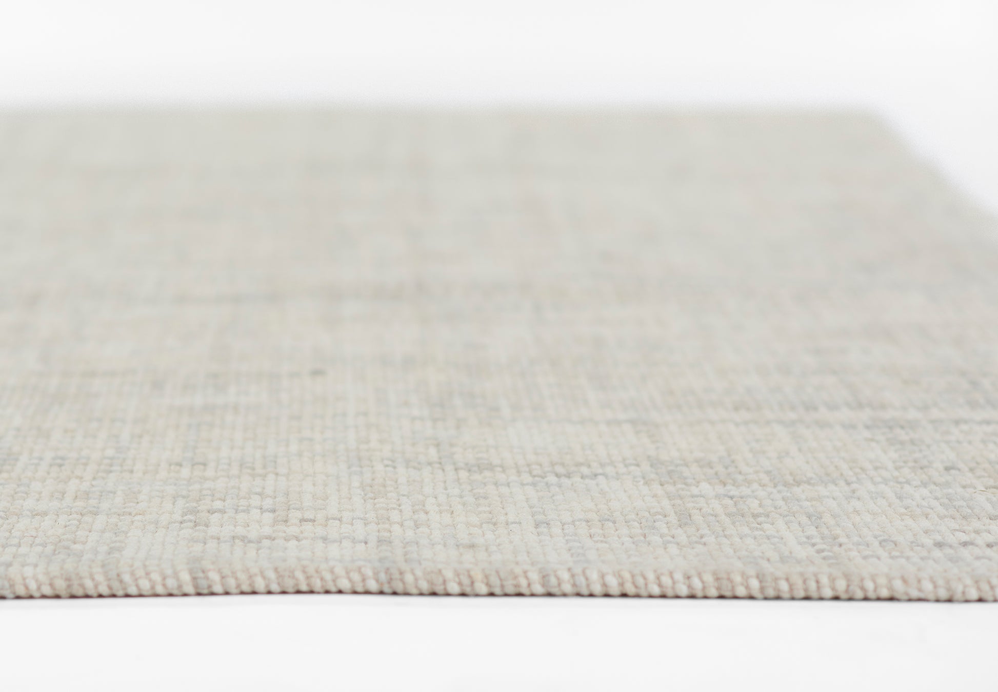 Beige flat-weave rug close-up with subtle grid texture; rectangular shape for living room or hallway.