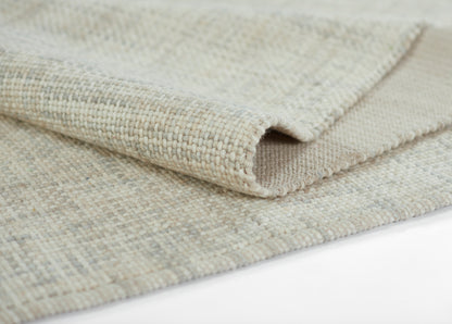Beige woven rug with speckled texture, folded corner showing tight, sturdy weave and neutral tones.