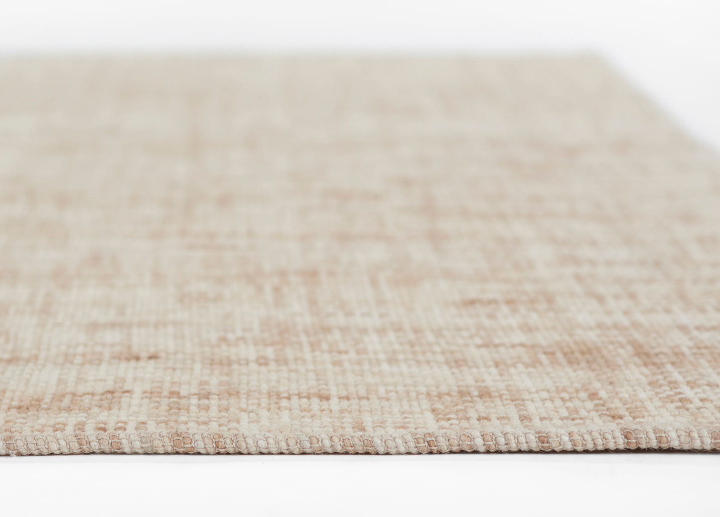 Beige flat-weave rug with natural fiber texture, close-up edge in soft pink-beige tones.