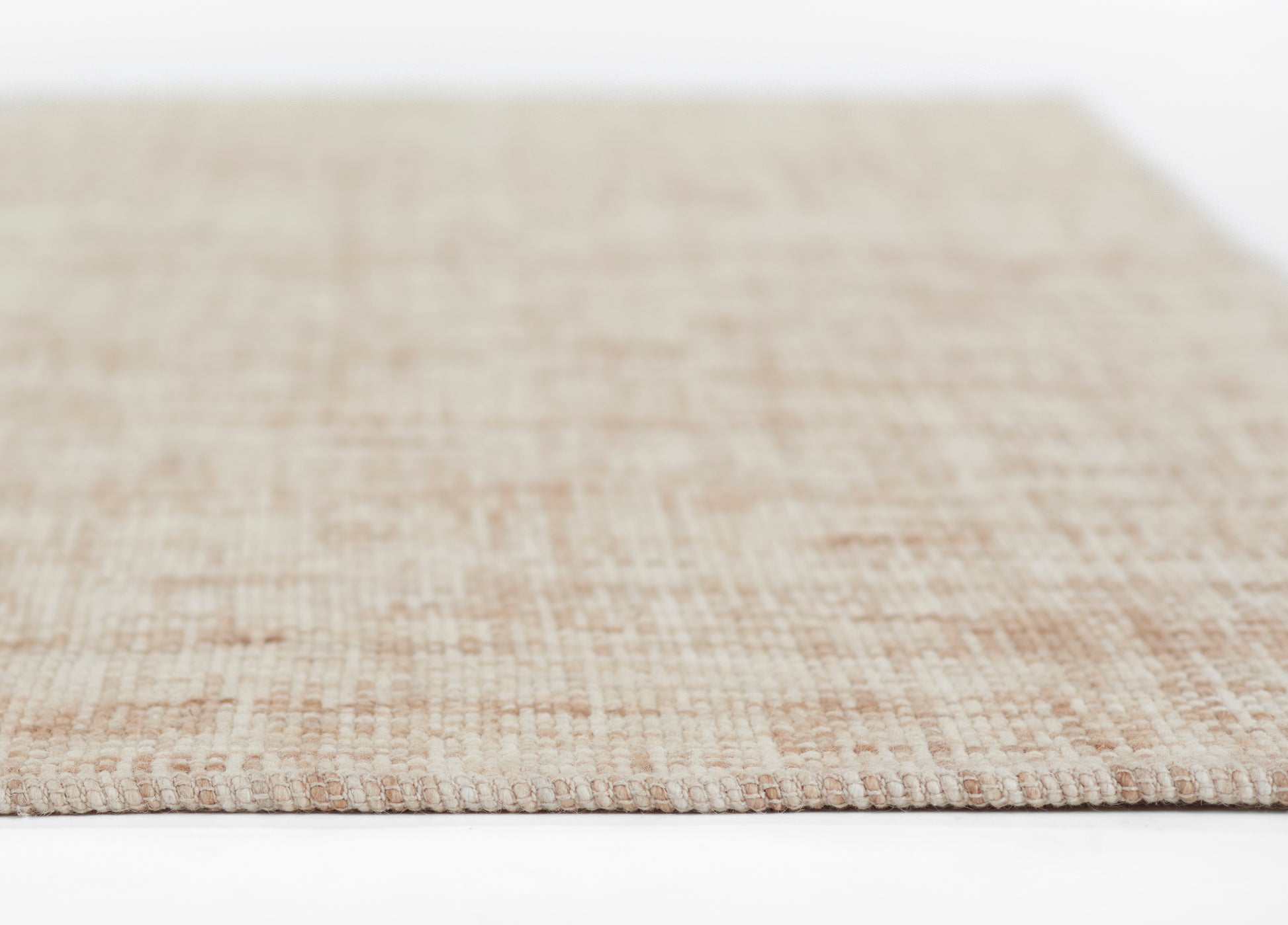 Beige flat-weave rug with natural fiber texture, close-up edge in soft pink-beige tones.