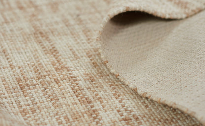 Beige natural-fiber woven rug close-up; warm cream tones, looped texture, rolled edge with suede backing.