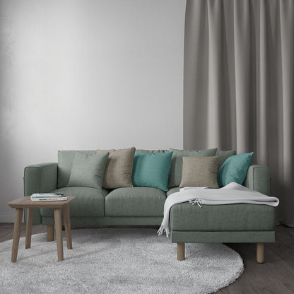 Teal-green sectional sofa with chaise, teal and beige cushions, wooden legs, small coffee table, grey rug, curtains.