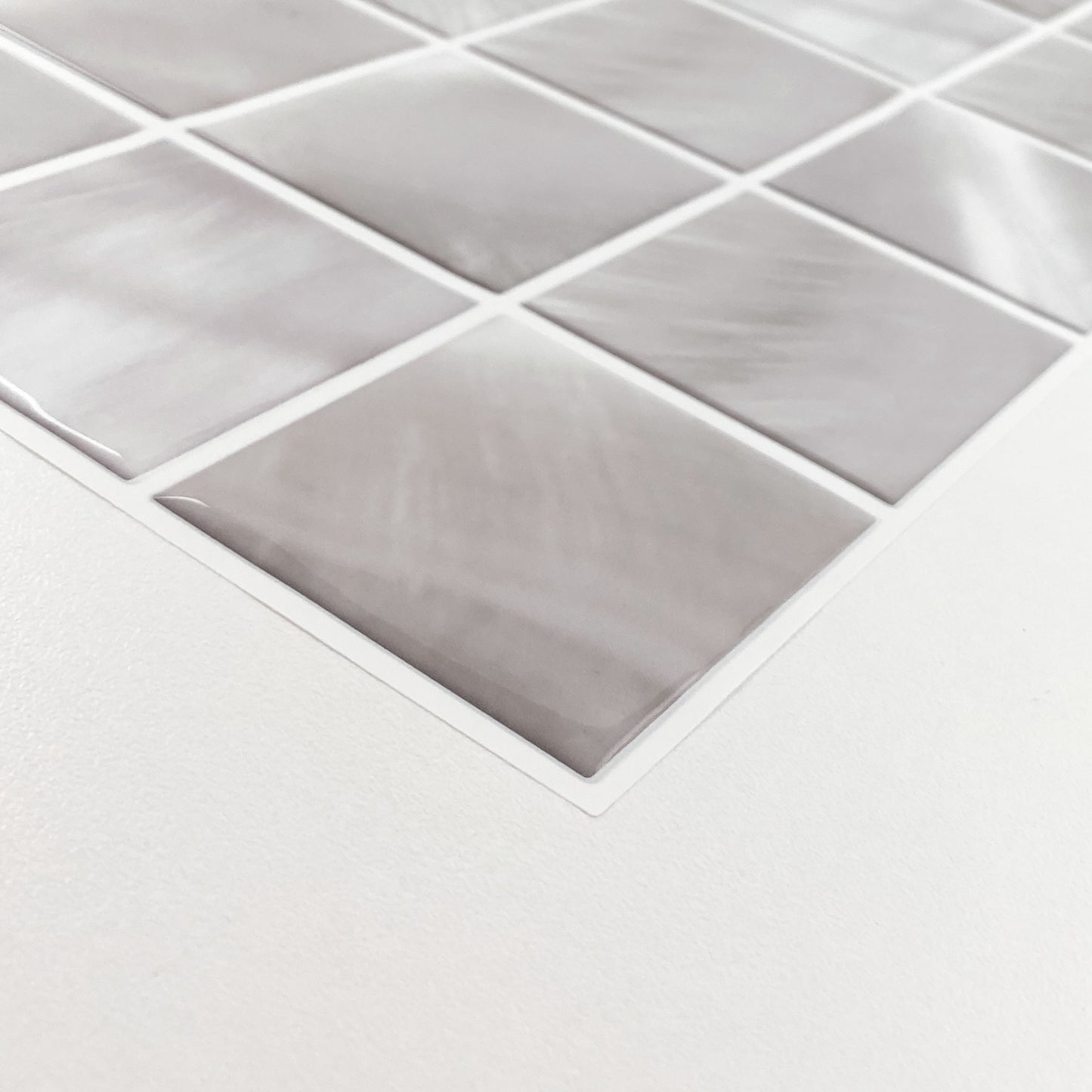 Close-up of light gray marble-pattern square tiles on a mesh sheet, angled on a white surface.