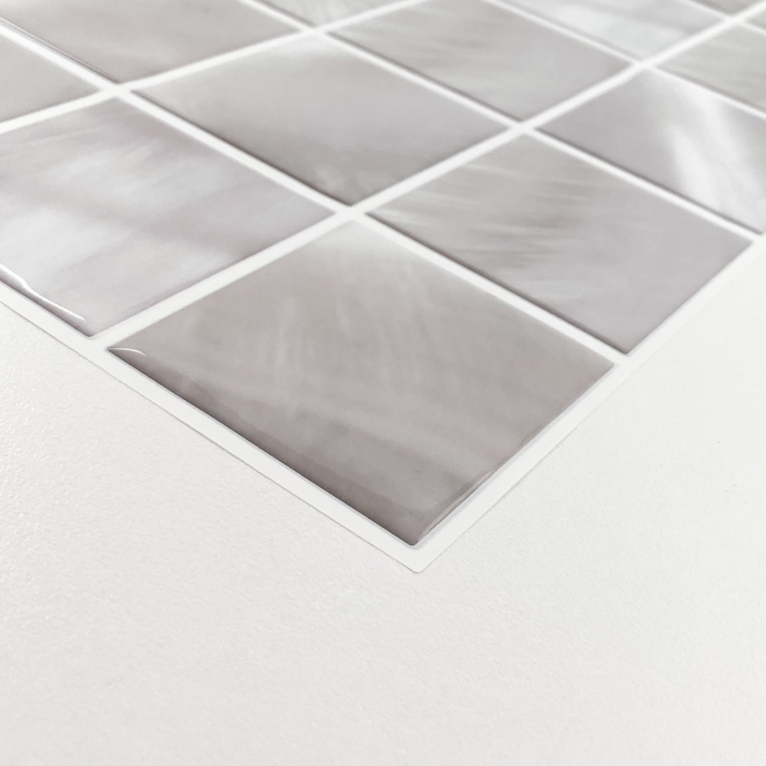 Close-up of light gray marble-pattern square tiles on a mesh sheet, angled on a white surface.