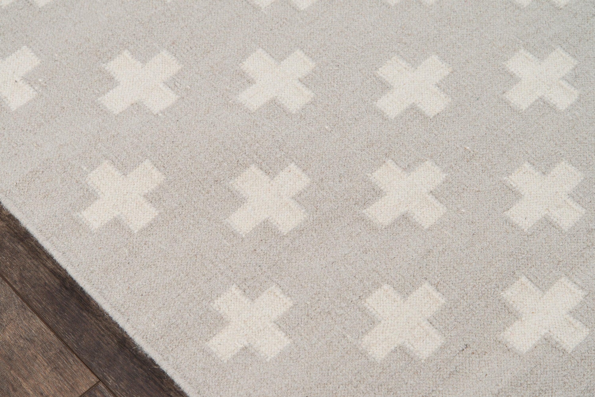 Gray area rug with white X motifs; soft plush pile on dark wood floor.