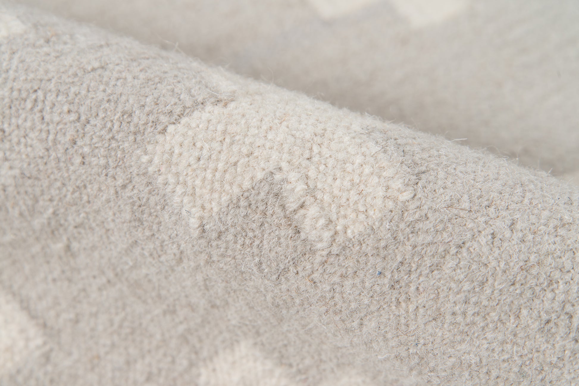 Close-up of light gray knitted fabric with fuzzy wool texture, sweater-style knit top.