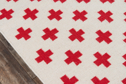 Cream rug with bold red cross motifs, repeating X pattern, edge on dark wood floor.