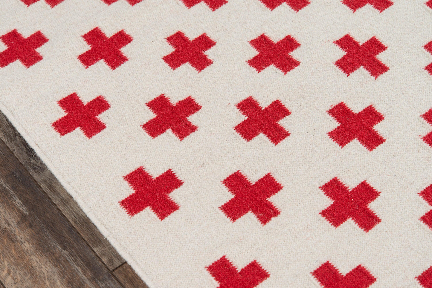 Cream textured rug with red X-shaped cross motifs on a wooden floor.