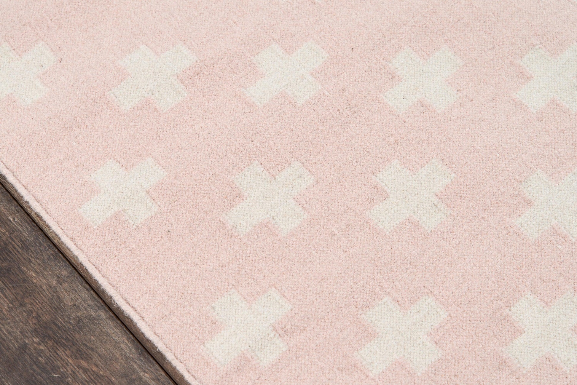 Pink area rug with white X-shaped motifs; plush texture on dark wood floor.