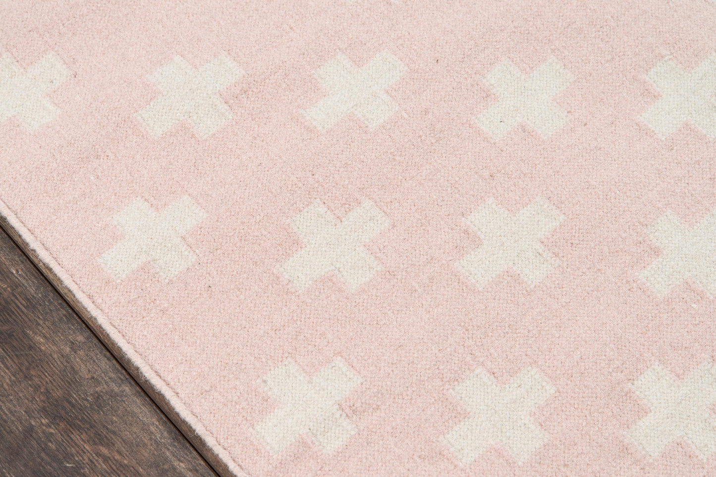 Soft pink rug with white X pattern on dark wood floor; plush fabric, rectangular area rug.