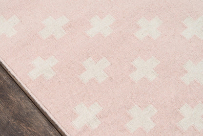 Soft pink rug with white X pattern on dark wood floor; plush fabric, rectangular area rug.