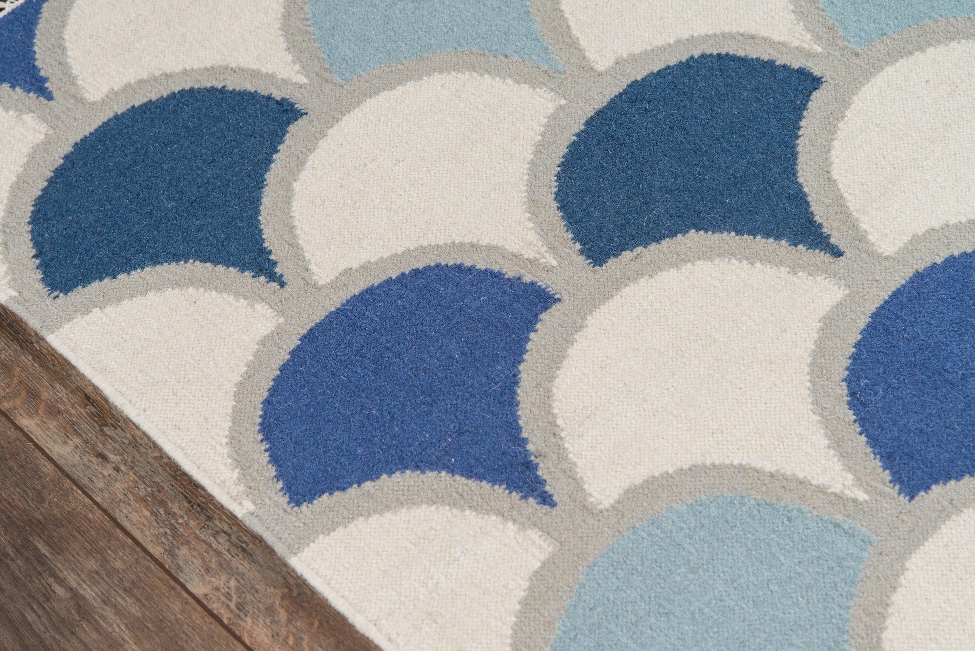 Textured rug with overlapping semicircles in blues and cream, gray outlines on a wood floor.