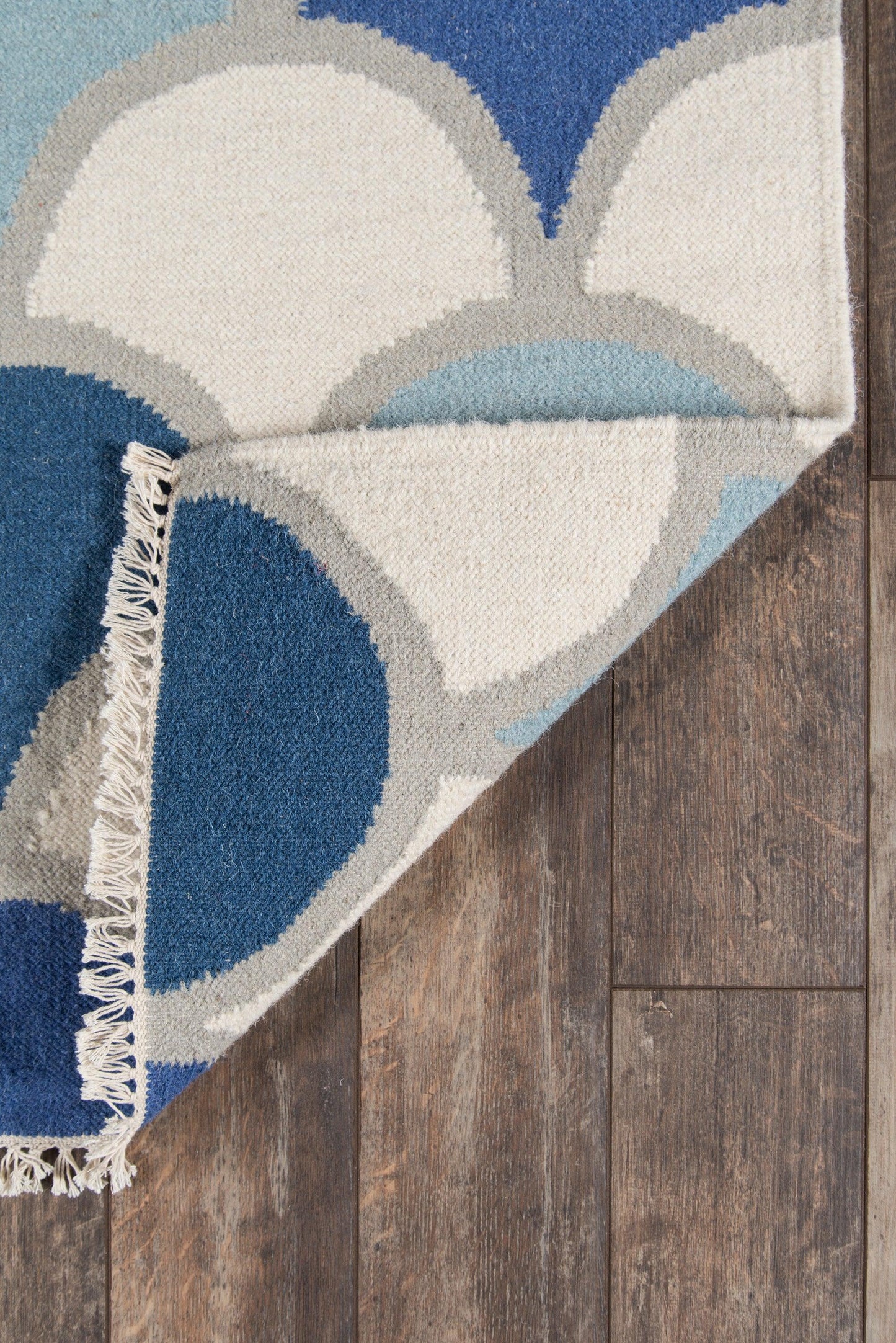 Abstract circular pattern area rug in blues, creams and grays with fringe on a wood floor