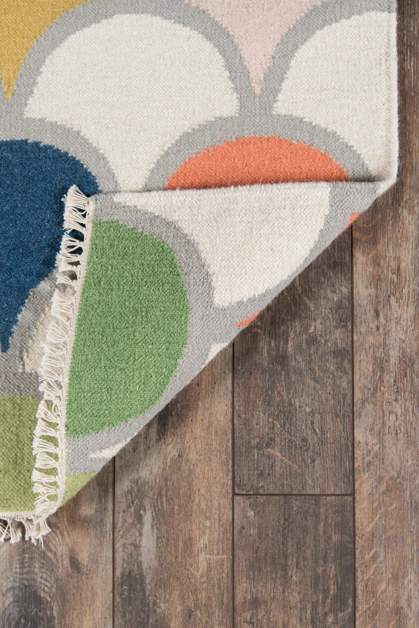 Geometric area rug with overlapping circles in cream, gray, yellow, orange, blue and green; fringed edge on wood floor