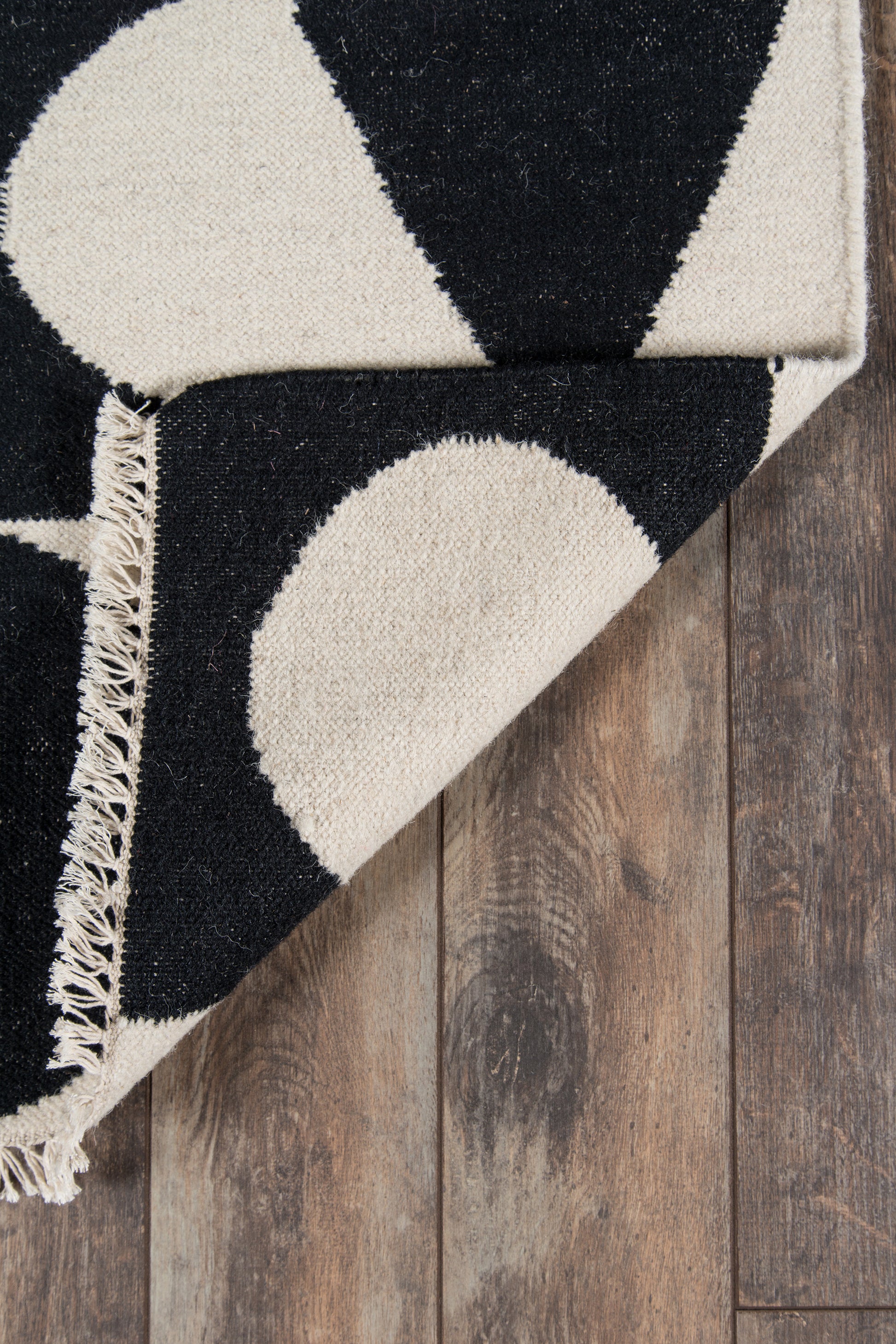 Geometric black and beige woven rug with large beige shapes and fringed edges on a wood floor