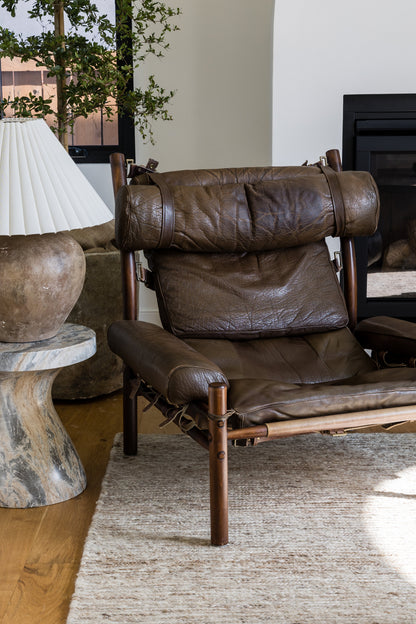 Brown leather lounge chair with wooden frame and padded headrest in a cozy living room.
