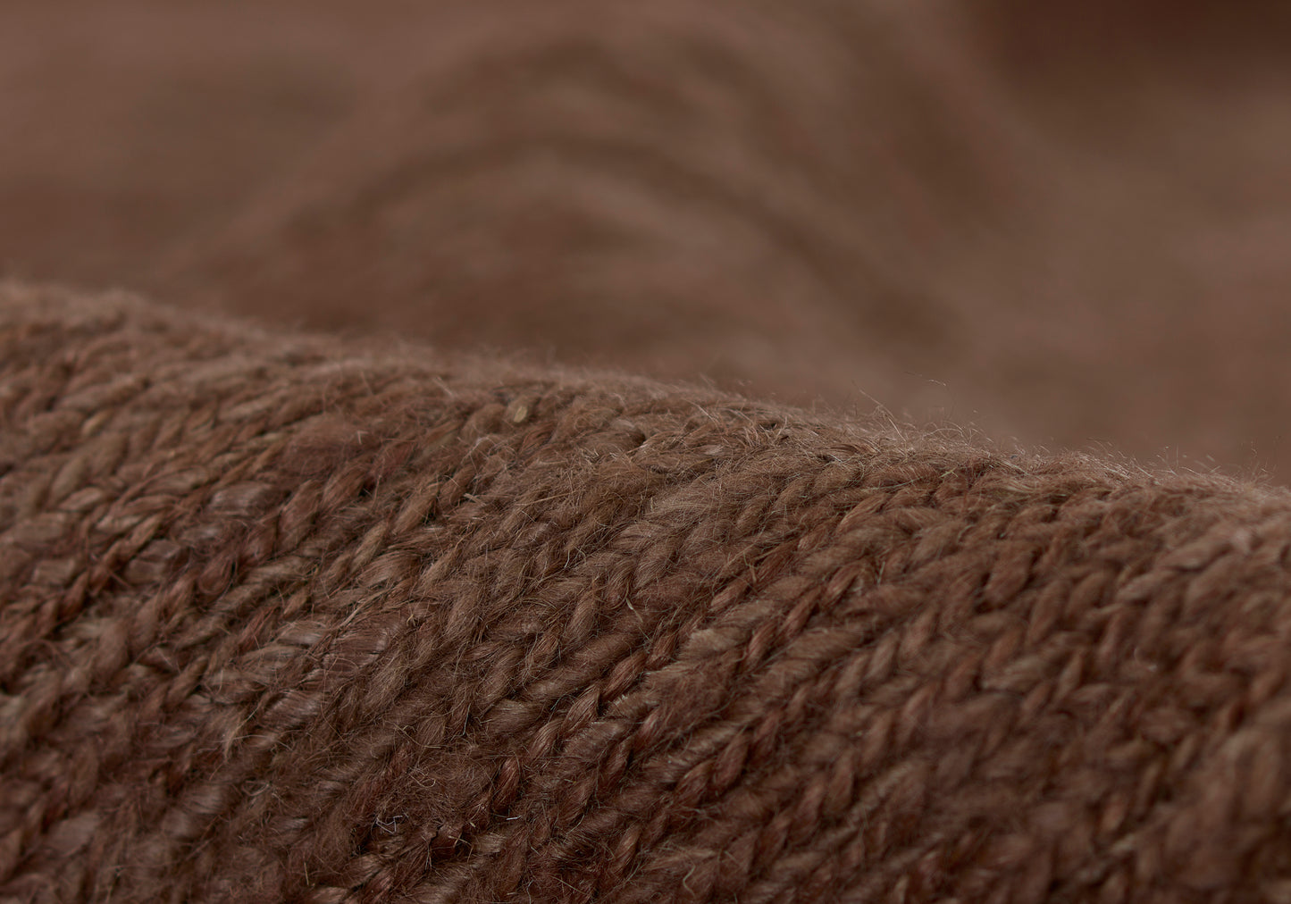 Close-up of brown knitted wool fabric with chunky yarn texture; cozy warm sweater or throw material.