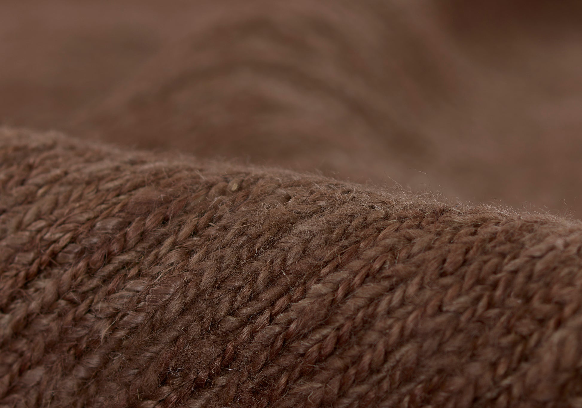 Close-up of brown knitted wool fabric with chunky yarn texture; cozy warm sweater or throw material.