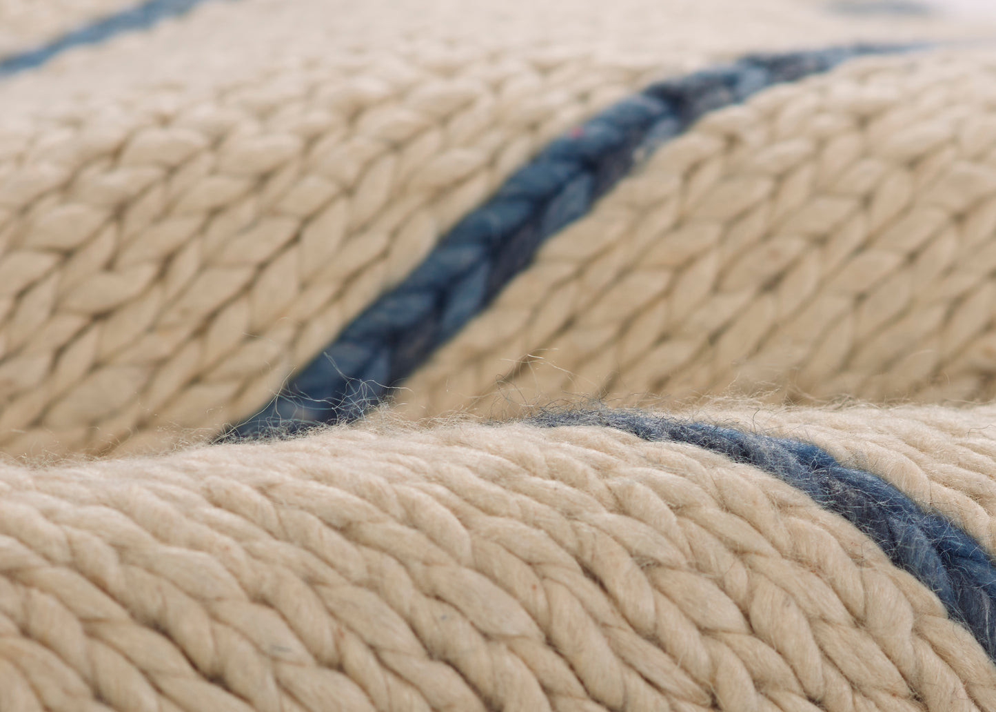 Close-up of a rug featuring a thick natural beige rope twine design with a dark blue stripe and braided textured fibers.