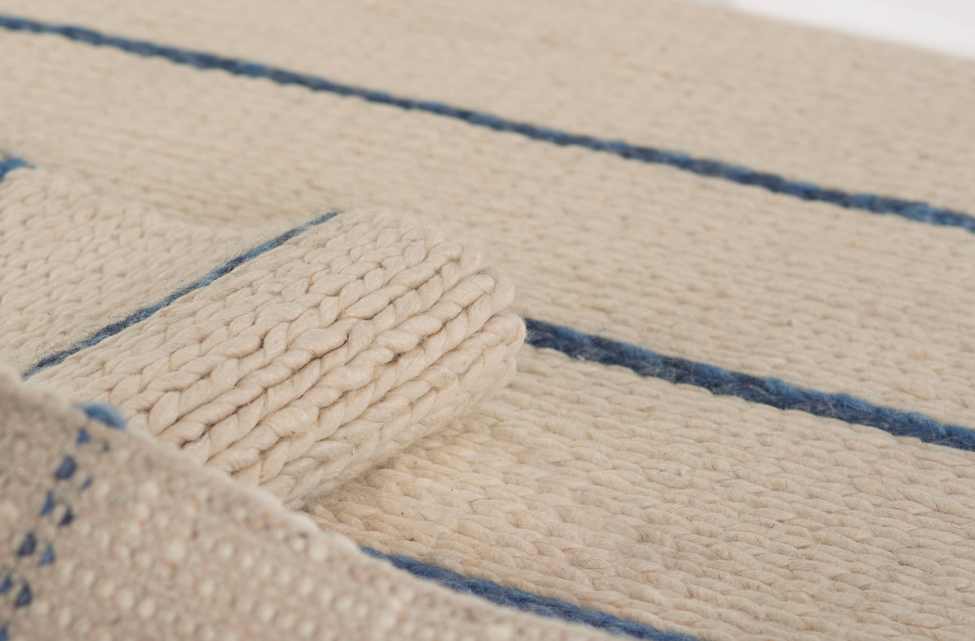Beige chunky woven rug with blue stripes; rolled edge and thick rope-like texture, casual coastal style.