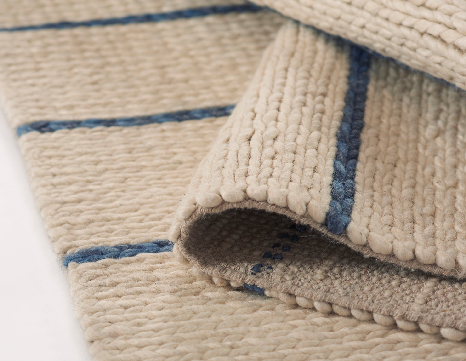 Beige loop-pile rug with blue stripes; natural woven texture, rolled corner reveals soft, cozy surface.