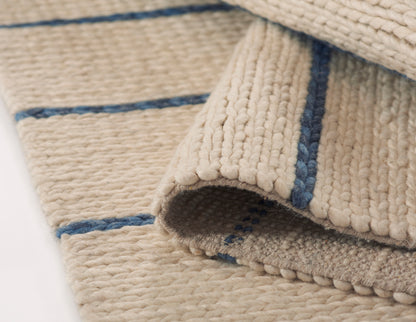 Beige loop-pile rug with blue stripes; natural woven texture, rolled corner reveals soft, cozy surface.