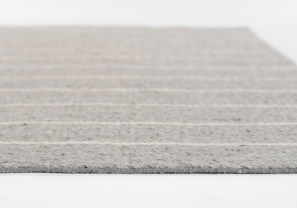 Grey striped area rug with soft woven texture, light and dark grey bands, visible edge fringe.
