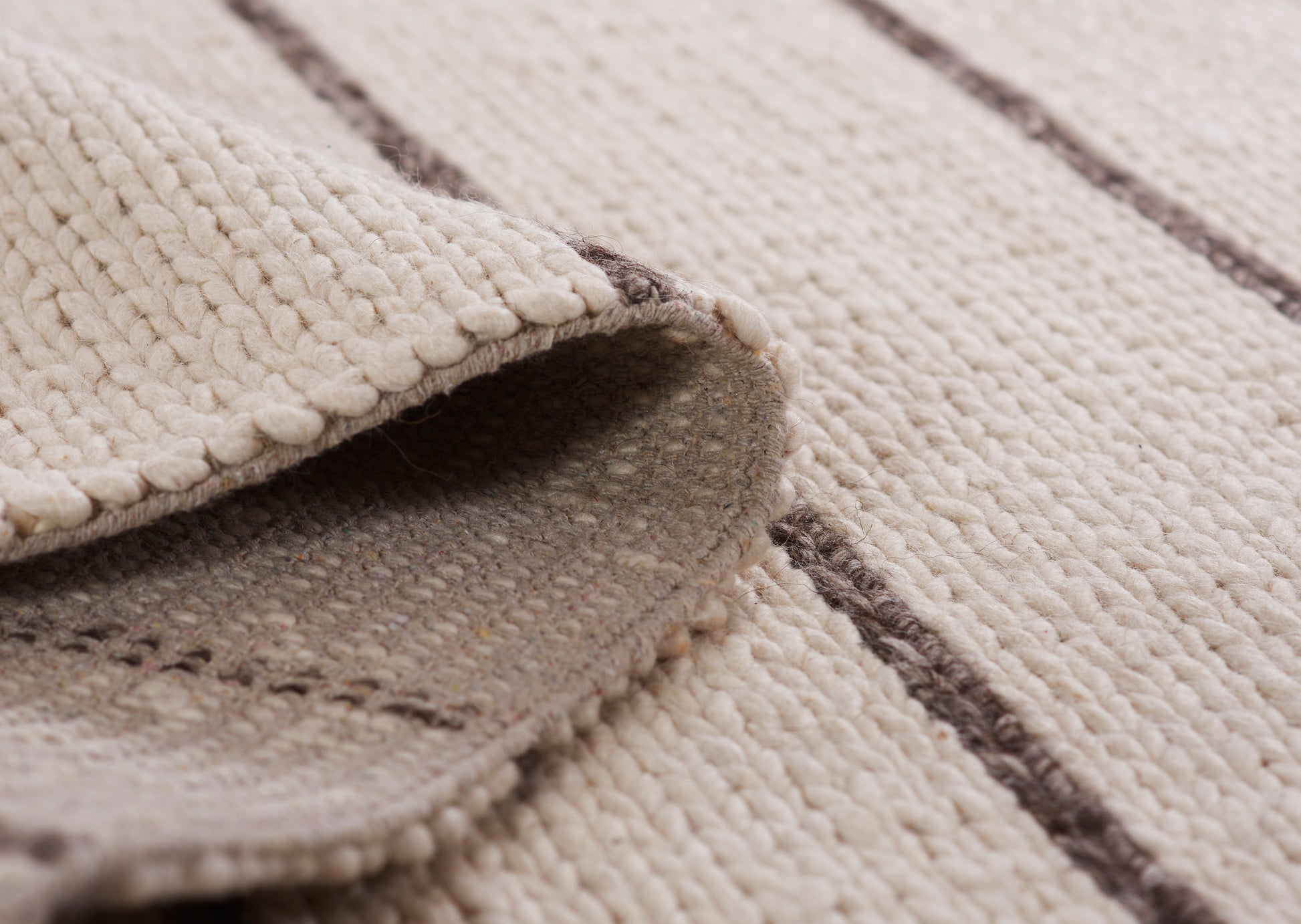 Beige woven rug with textured loop pile and dark brown stripes; 5' x 8' rug; folded edge reveals soft underside.
