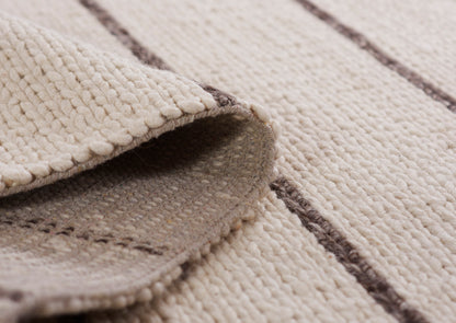 Beige woven rug with textured loop pile and dark brown stripes; 5' x 8' rug; folded edge reveals soft underside.