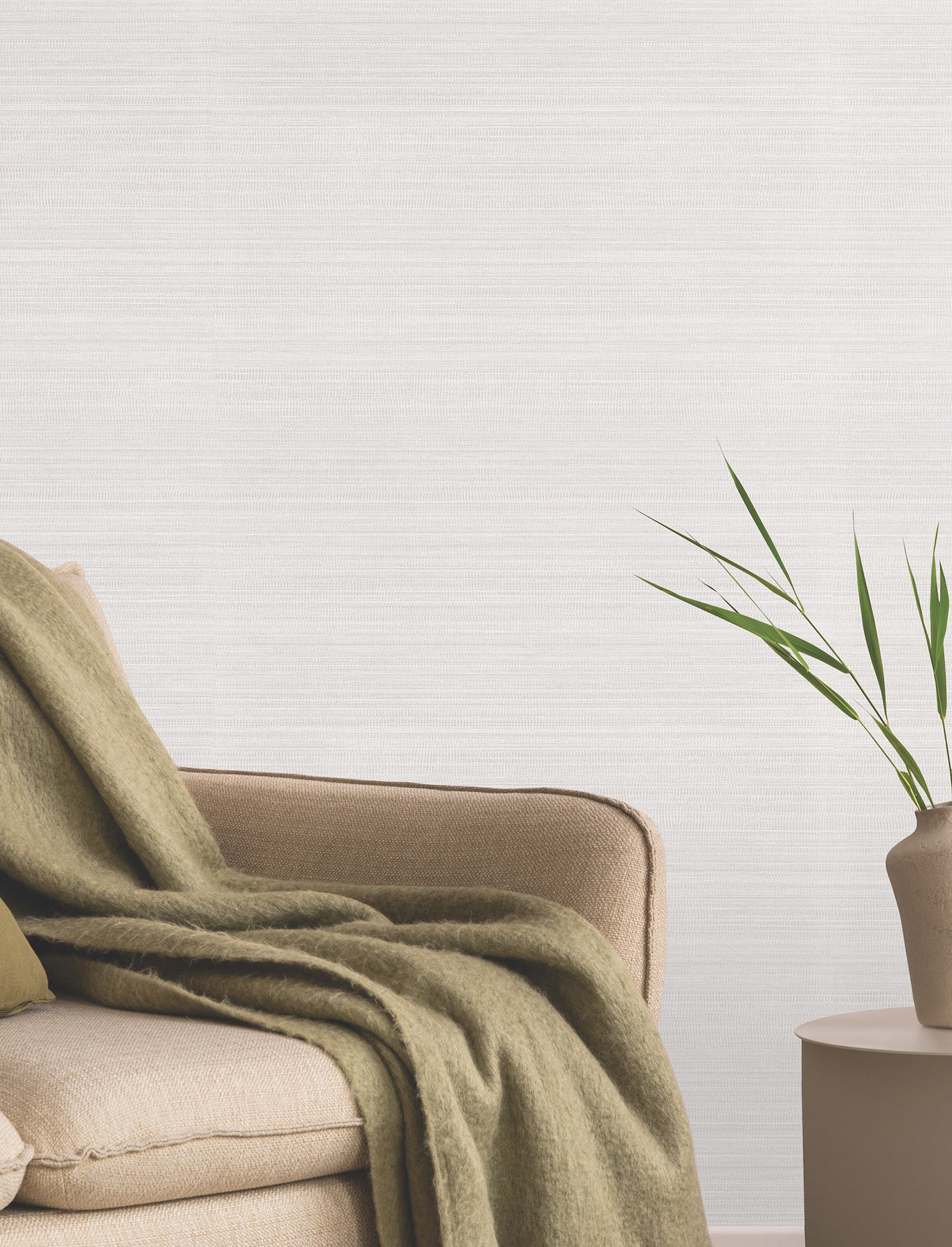 Neutral living room with grey-toned wallpaper, beige sofa with olive-green throw, a round side table and a potted plant.