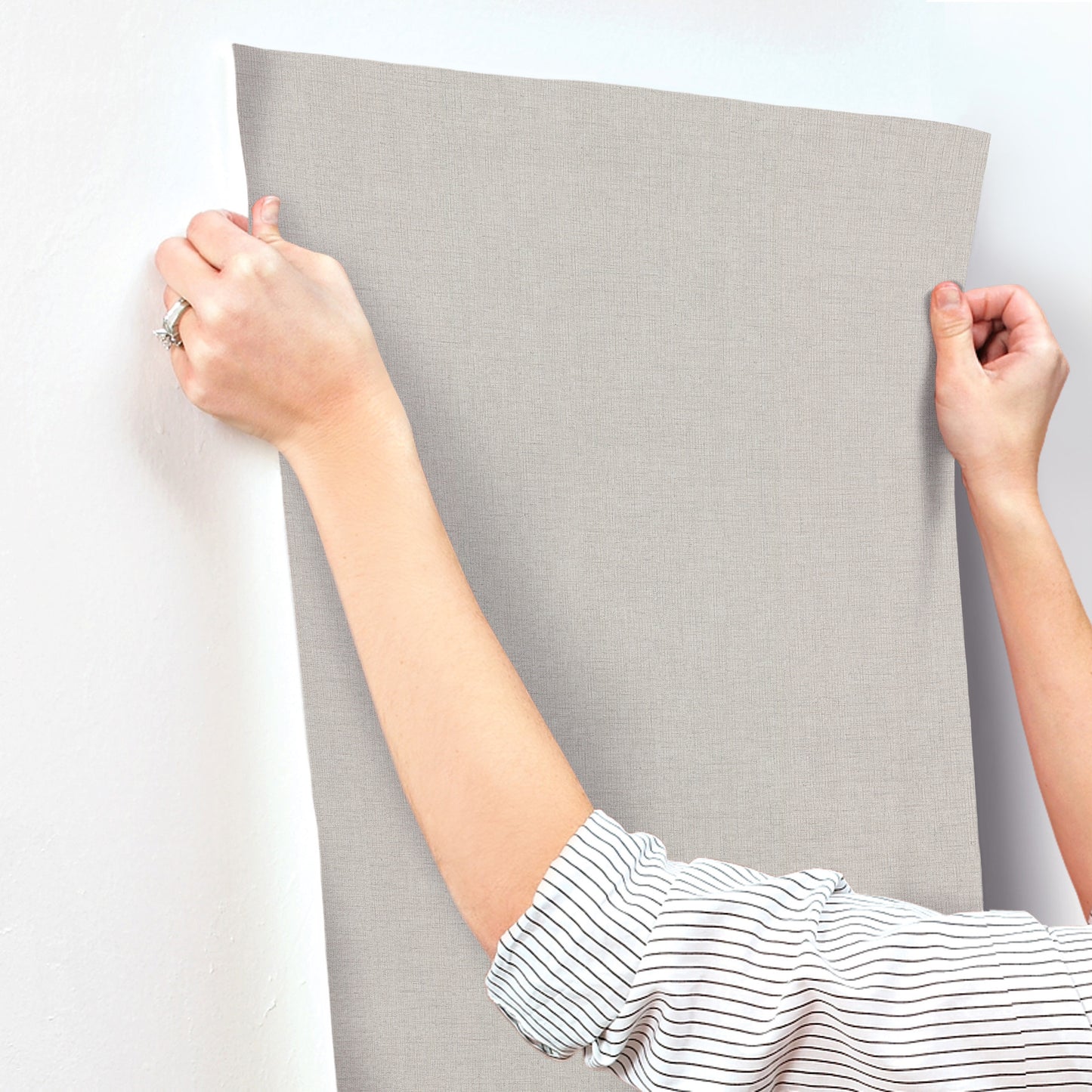 Rectangular, light gray linen-textured wallpaper being held by hands.