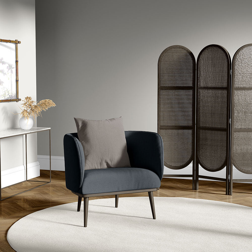 Graphite solid upholstery fabric on a dark gray armchair with a light beige cushion, wooden legs, in a modern living room with a three-panel woven screen and a circular rug