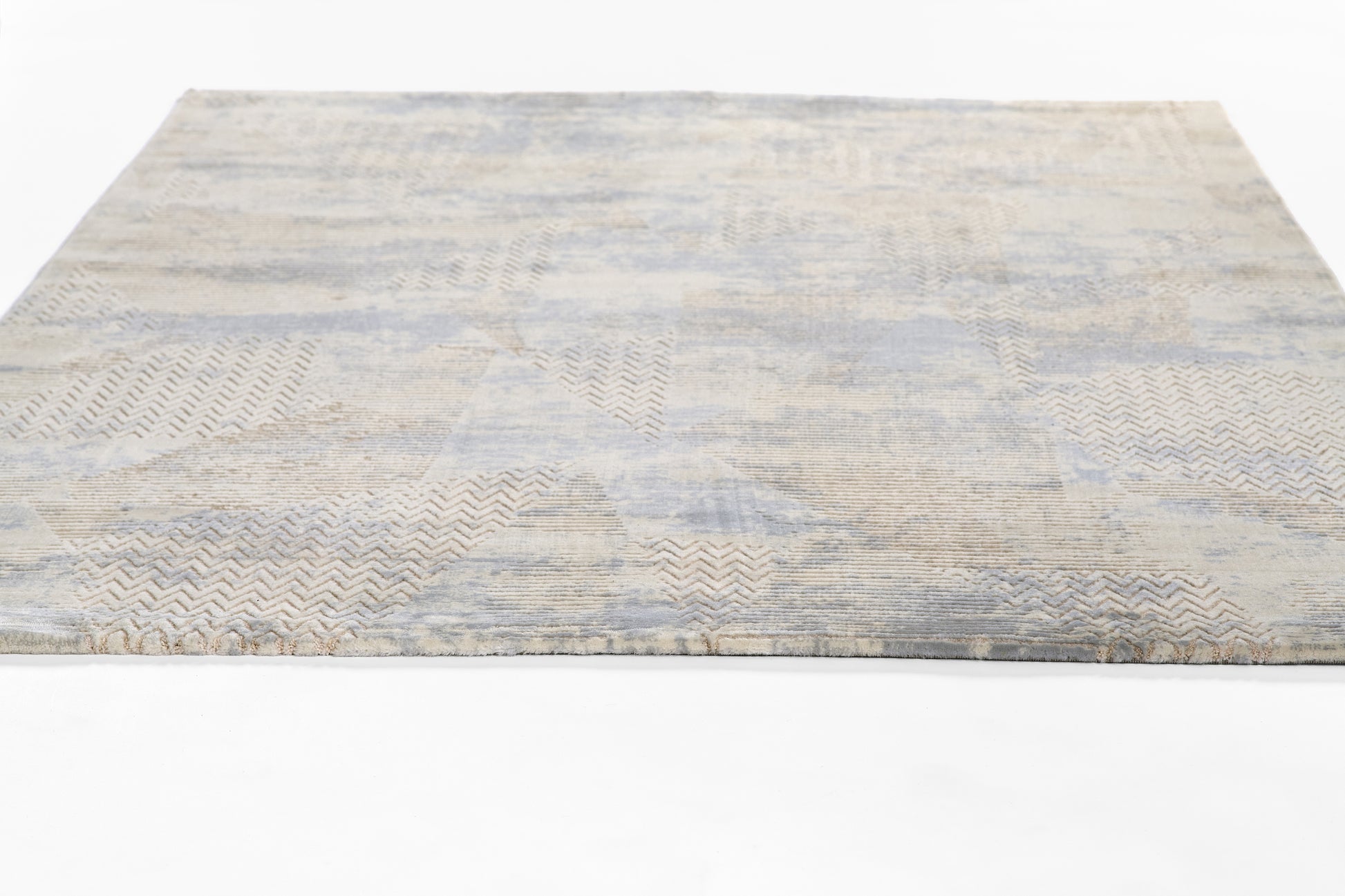 Rectangular area rug in pale blue, beige and gray with patchwork geometric pattern and subtle chevrons.