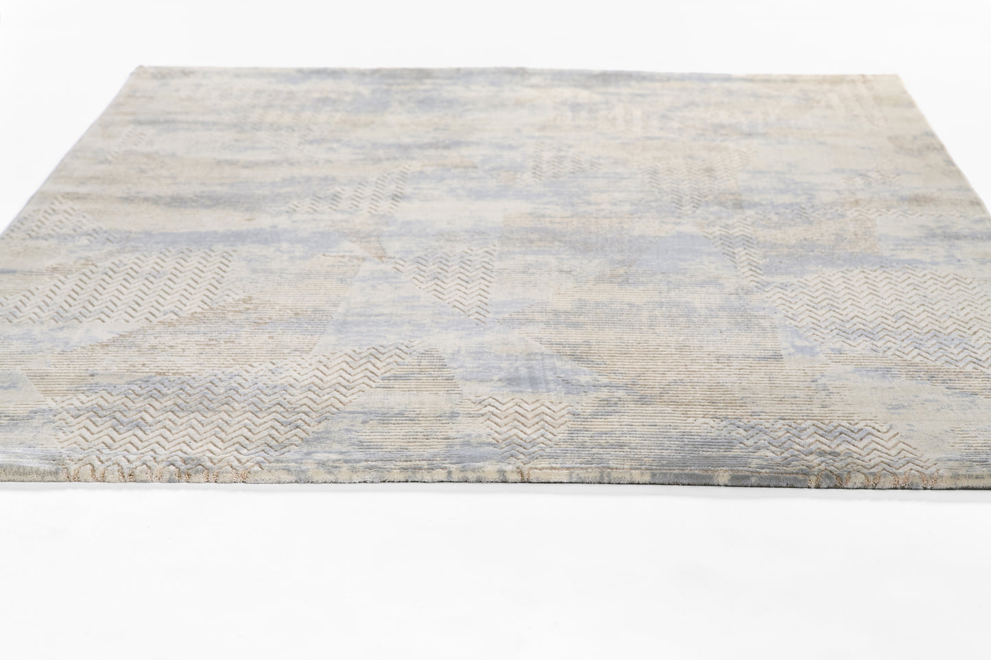 Light blue-gray and beige abstract area rug with chevron patchwork; soft woven texture, rectangular.