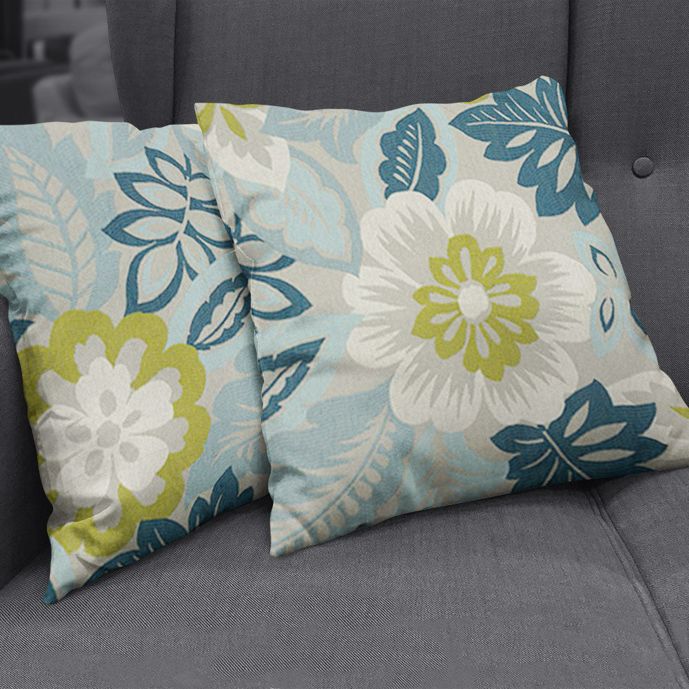 Two decorative throw pillows featuring blue, teal and lime floral patterns on light gray fabric, resting on a gray sofa.