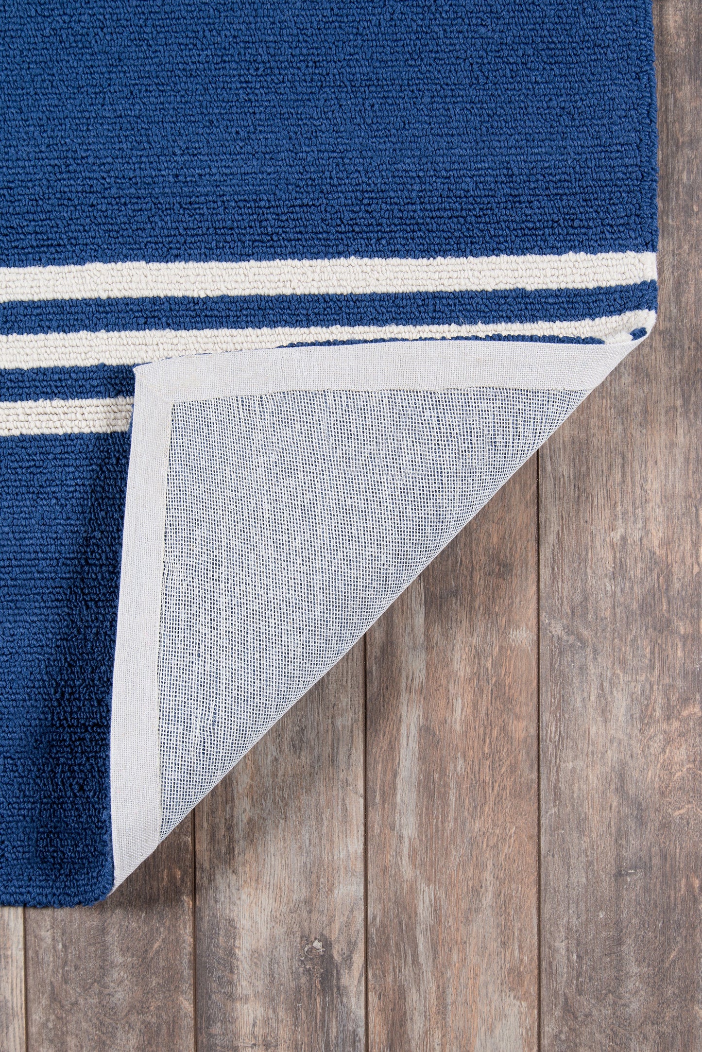 Navy blue rug with white striped edge; folded corner reveals light gray underside and woven texture on wood floor.