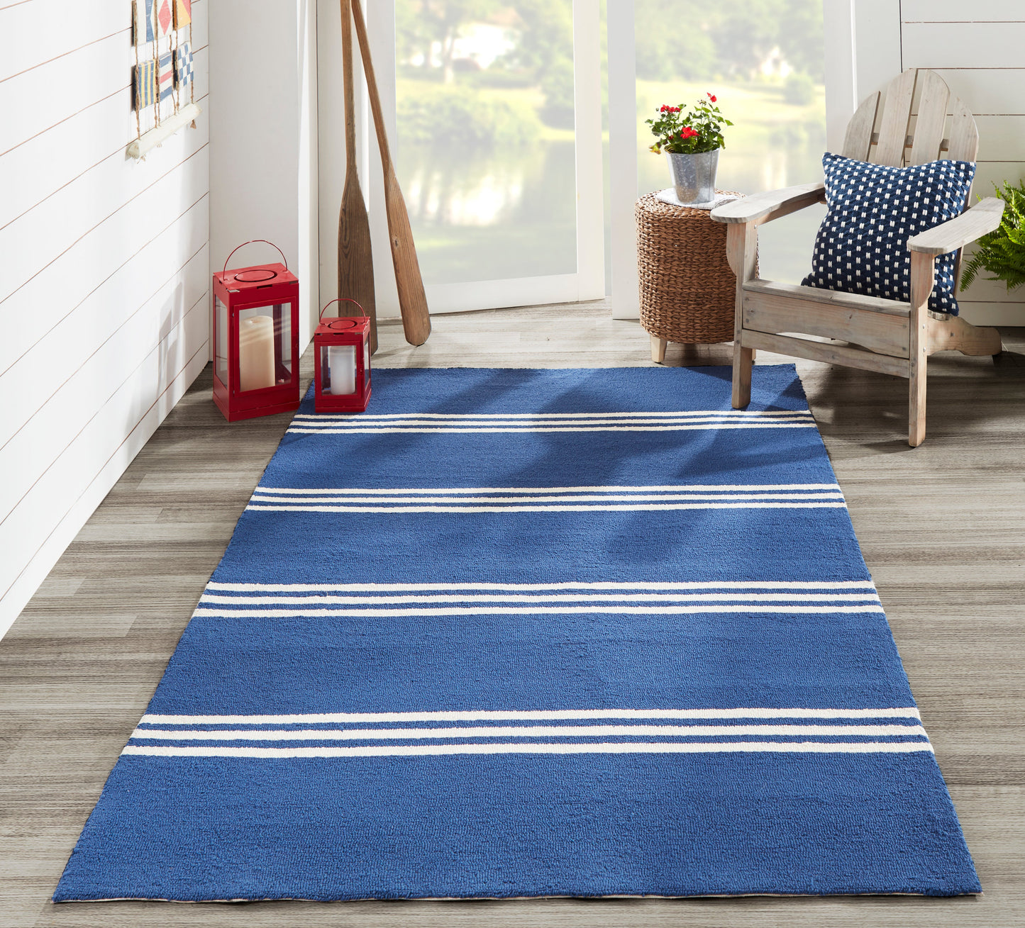 Blue striped area rug on wood floor by window, with red lanterns, oars, wicker table, and wooden chair with navy cushion.