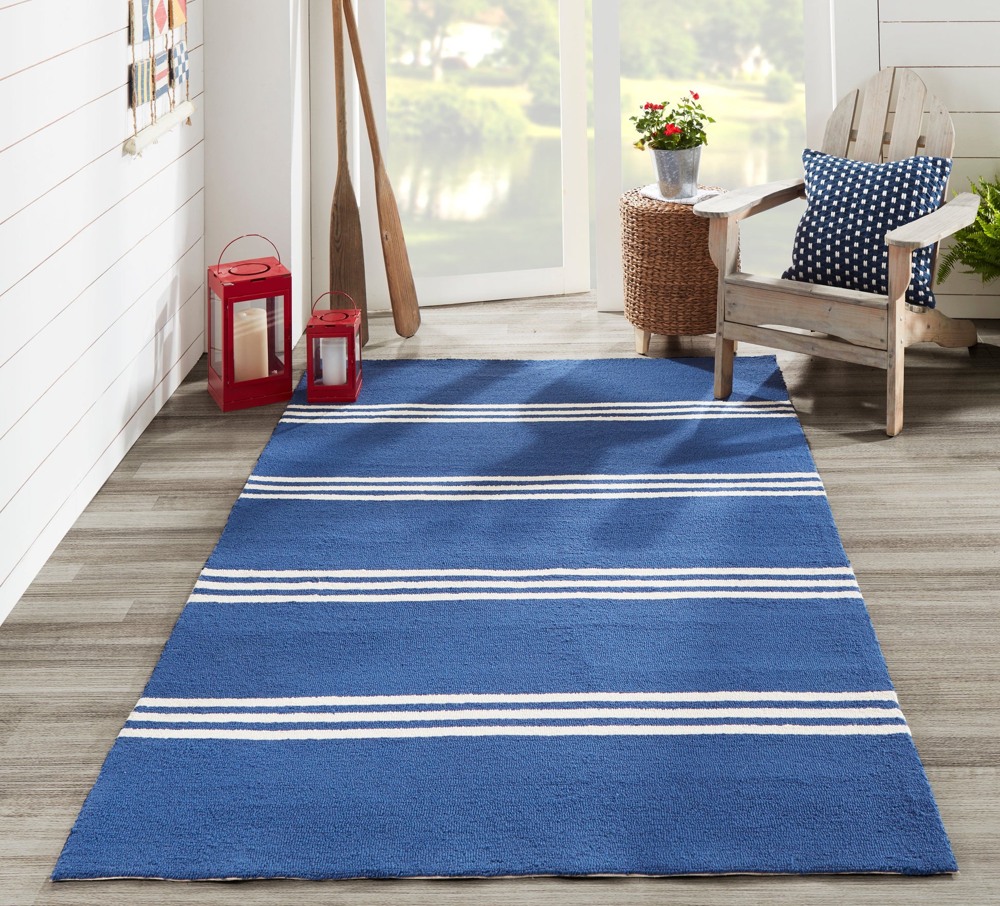 Blue rectangular coastal rug with white stripes on wood floor beside red lanterns and a wicker chair.