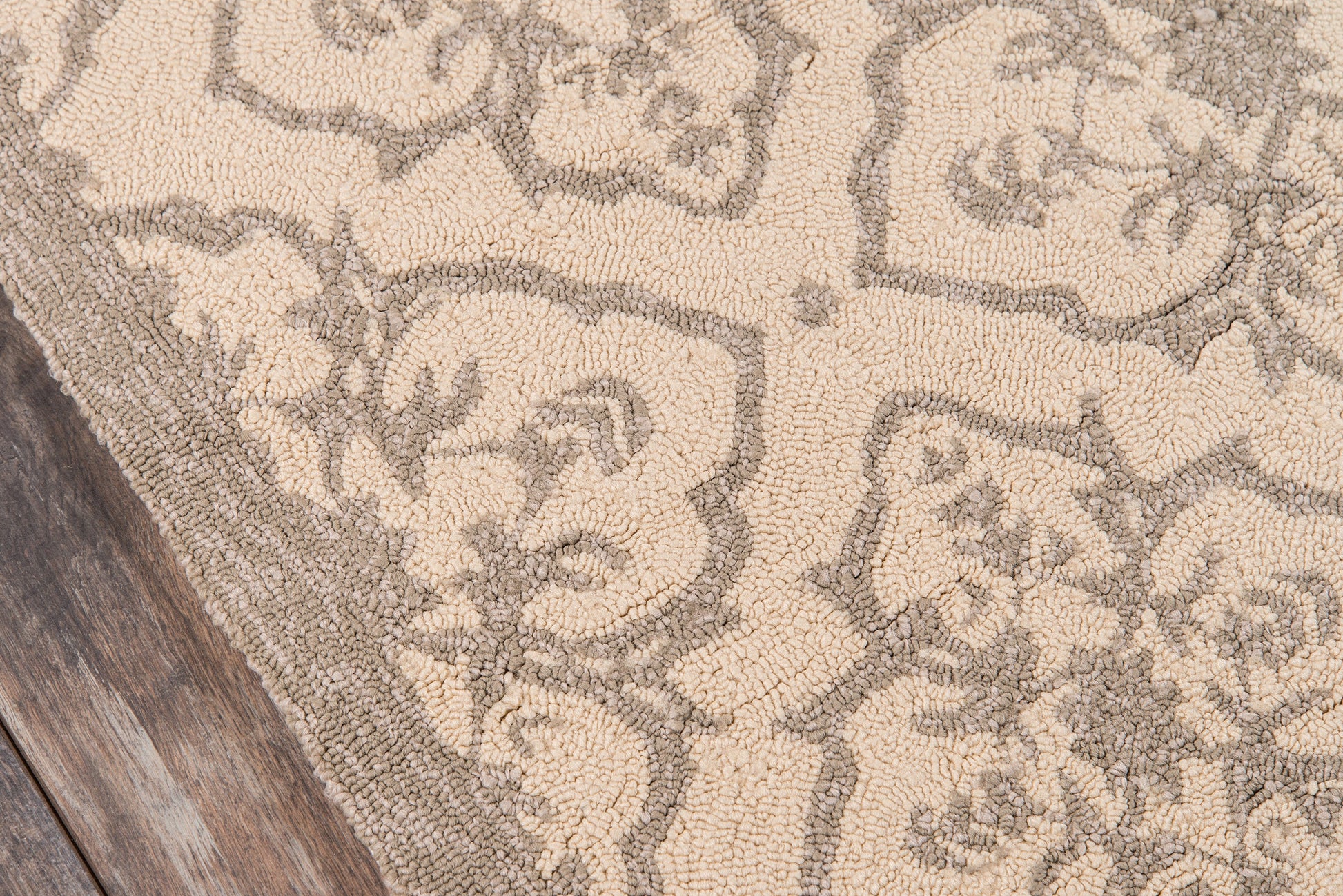 Beige area rug with taupe damask floral pattern on wooden floor.