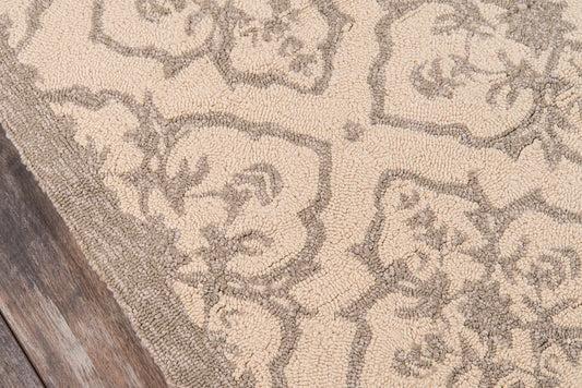 Beige area rug with taupe damask floral pattern on wooden floor.