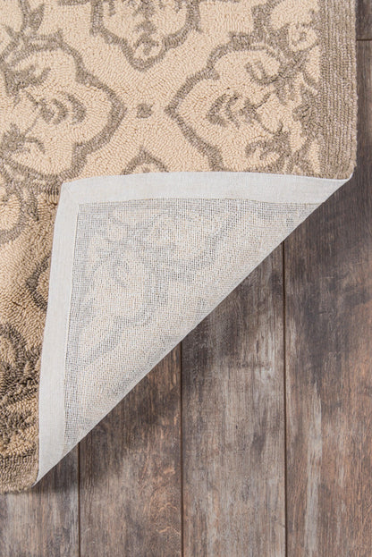 Taupe & tan ornate damask rug; corner lifted to reveal light woven backing, on wood floor.