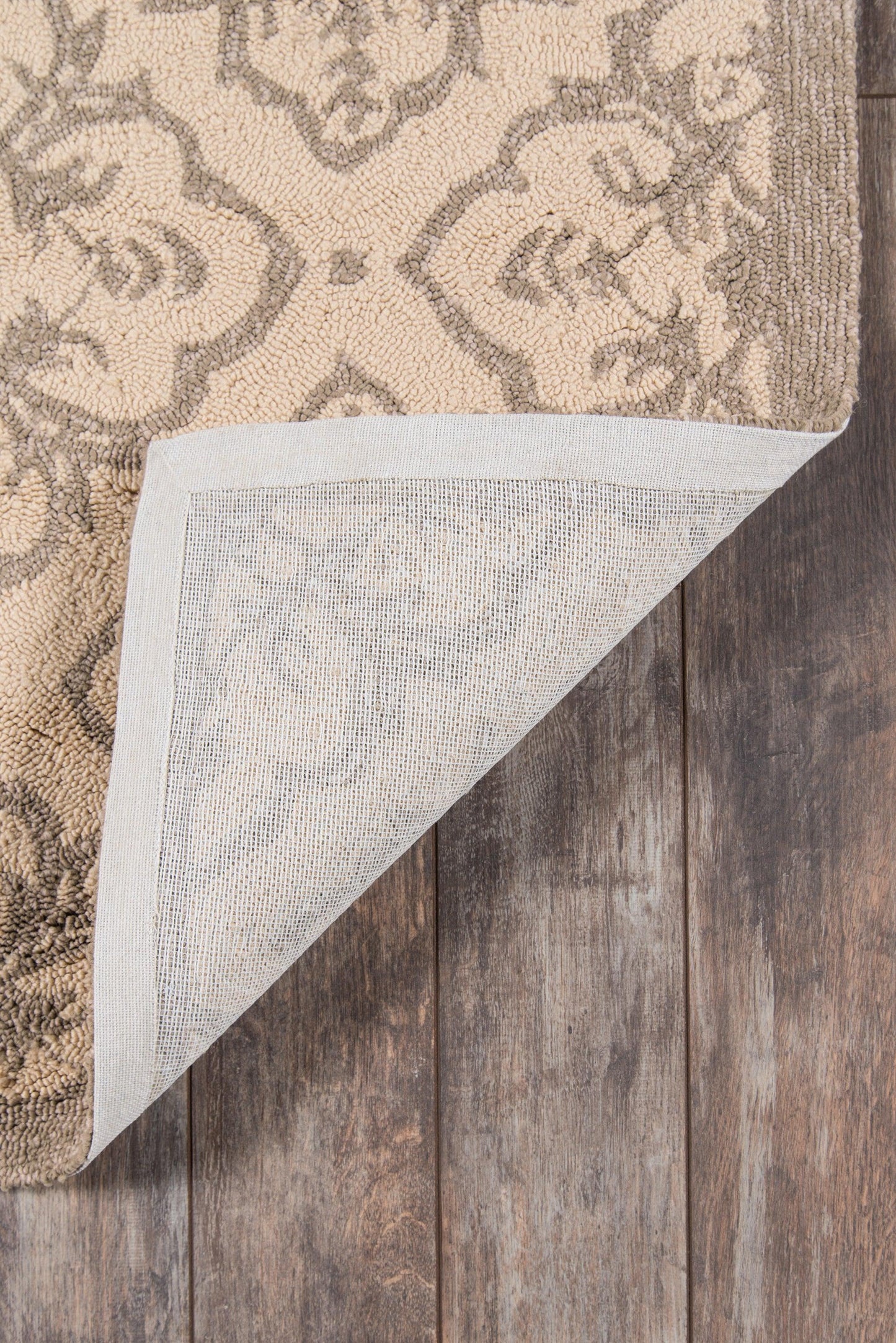 Taupe and beige patterned area rug with a woven backing, corner folded to show underside, on wood floor.