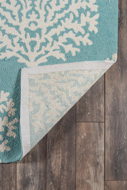 Teal rug with white coral-like pattern, corner folded to reveal pale underside on dark wooden floor.