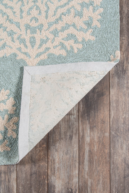 Teal-blue patterned area rug with beige ornamental motif; folded corner shows light backing on wooden floor.